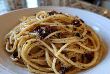 Close-up of creamy caramelized onion pasta tossed with herbs and dark bits of onion in a white bowl.