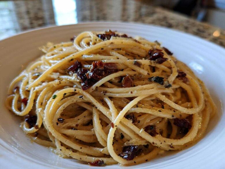 Close-up of creamy caramelized onion pasta tossed with herbs and dark bits of onion in a white bowl.