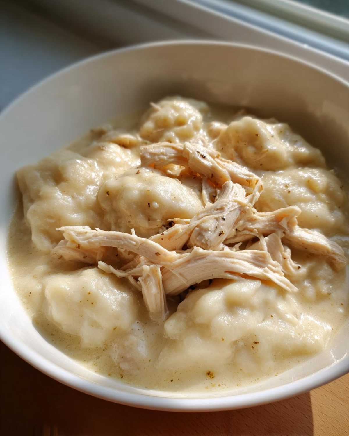 Close-up of a creamy bowl of homemade chicken and dumplings topped with shredded chicken.