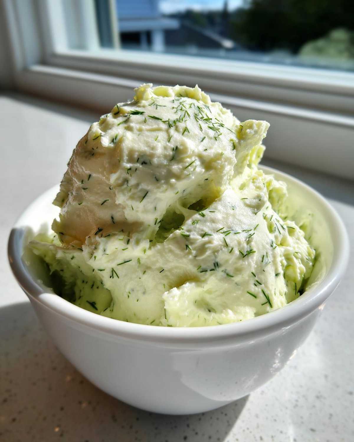 A white bowl filled with thick, creamy dill dip generously sprinkled with fresh chopped dill.