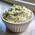 A close-up of thick, creamy dill dip garnished with fresh dill sprigs, served in a white bowl.