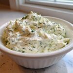 A close-up of thick, creamy dill dip generously mixed with fresh green dill, served in a white bowl.