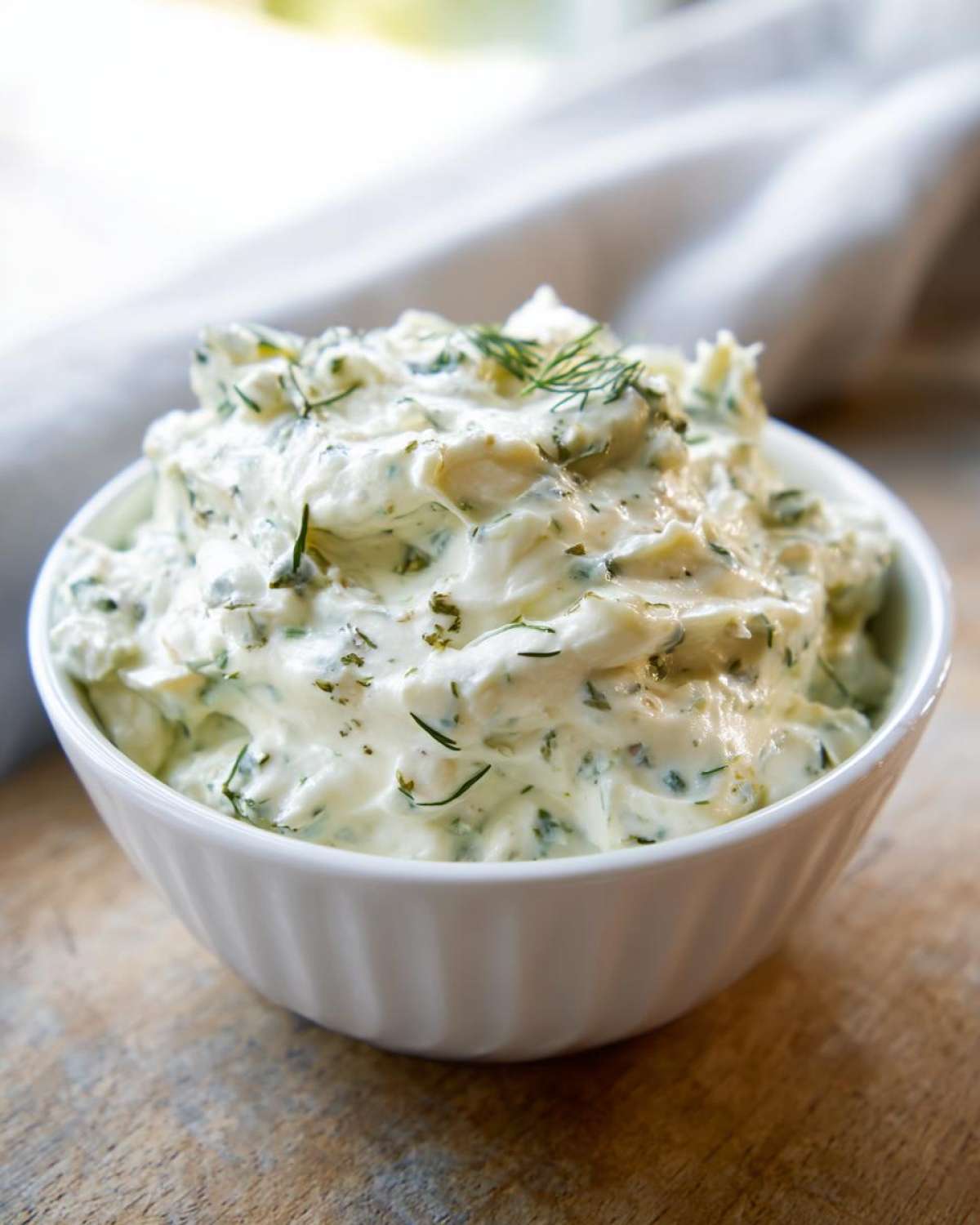 Close-up of creamy dill pickle dip mixed with fresh herbs, served in a small white bowl.
