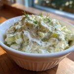 Close-up of creamy dill pickle dip, featuring chopped pickles and fresh dill, served in a white bowl.