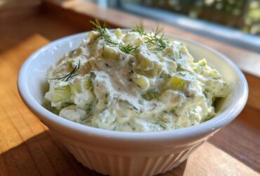 Close-up of creamy dill pickle dip, featuring chopped pickles and fresh dill, served in a white bowl.