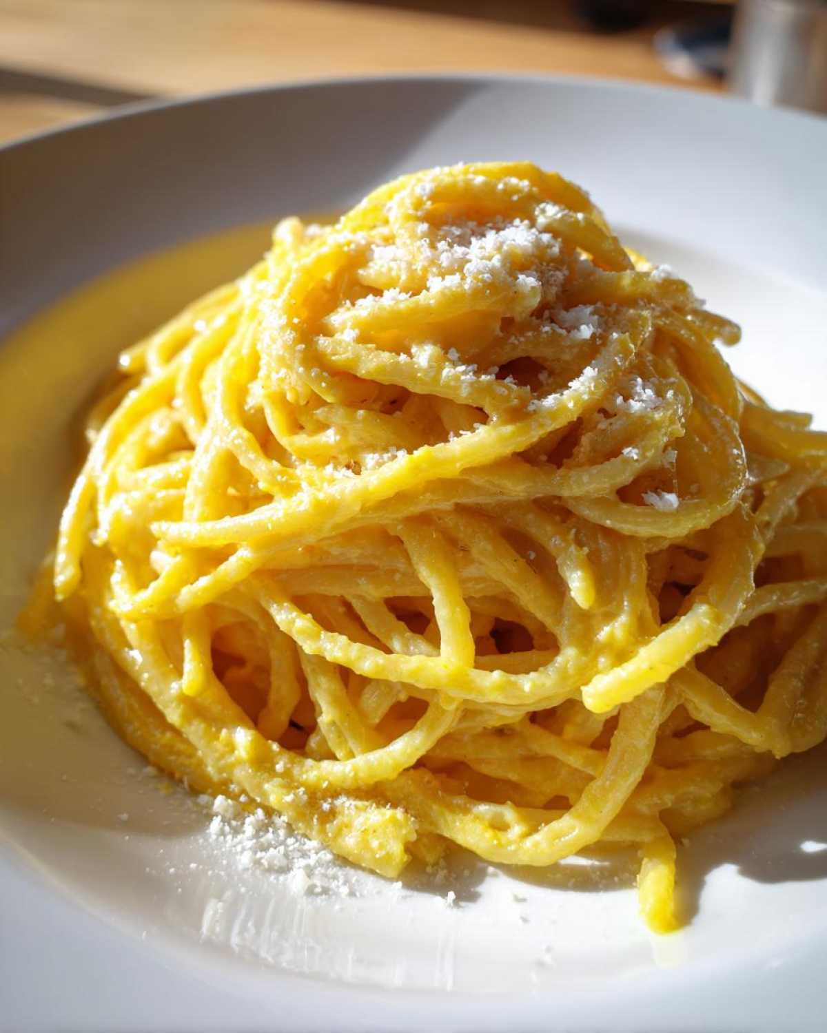 A close-up shot of a perfectly twirled mound of creamy lemon pasta, topped with grated Parmesan cheese, served on a white plate.