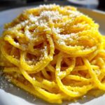 A vibrant close-up of creamy lemon pasta tossed in a bright yellow sauce and topped with grated cheese.