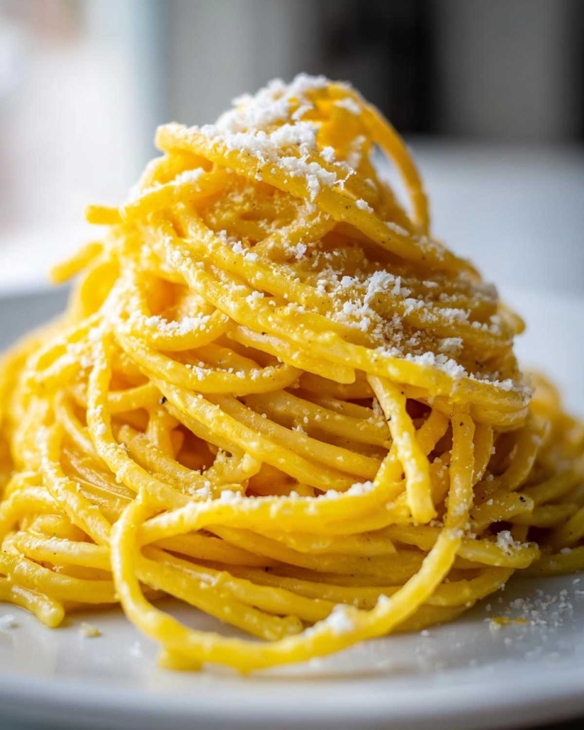A tall mound of bright yellow creamy lemon pasta topped with grated Parmesan cheese on a white plate.
