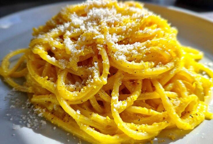 A vibrant close-up of creamy lemon pasta tossed in a bright yellow sauce and topped with grated cheese.