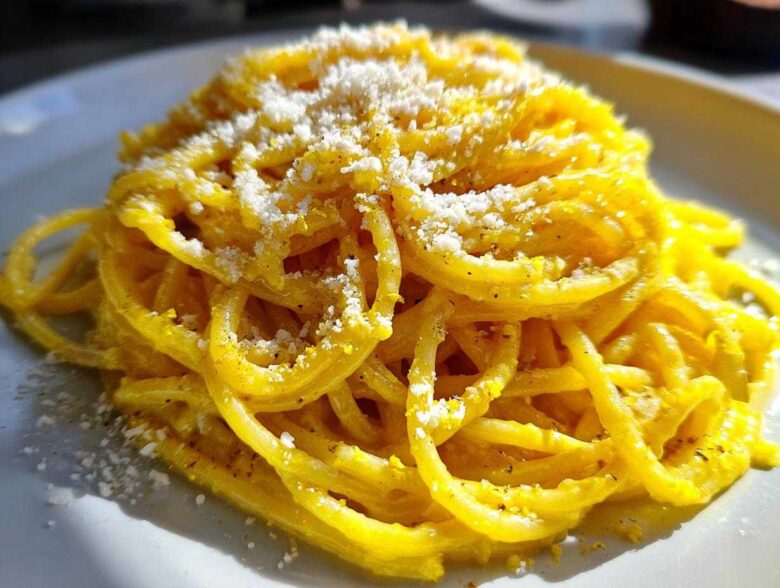 A vibrant close-up of creamy lemon pasta tossed in a bright yellow sauce and topped with grated cheese.