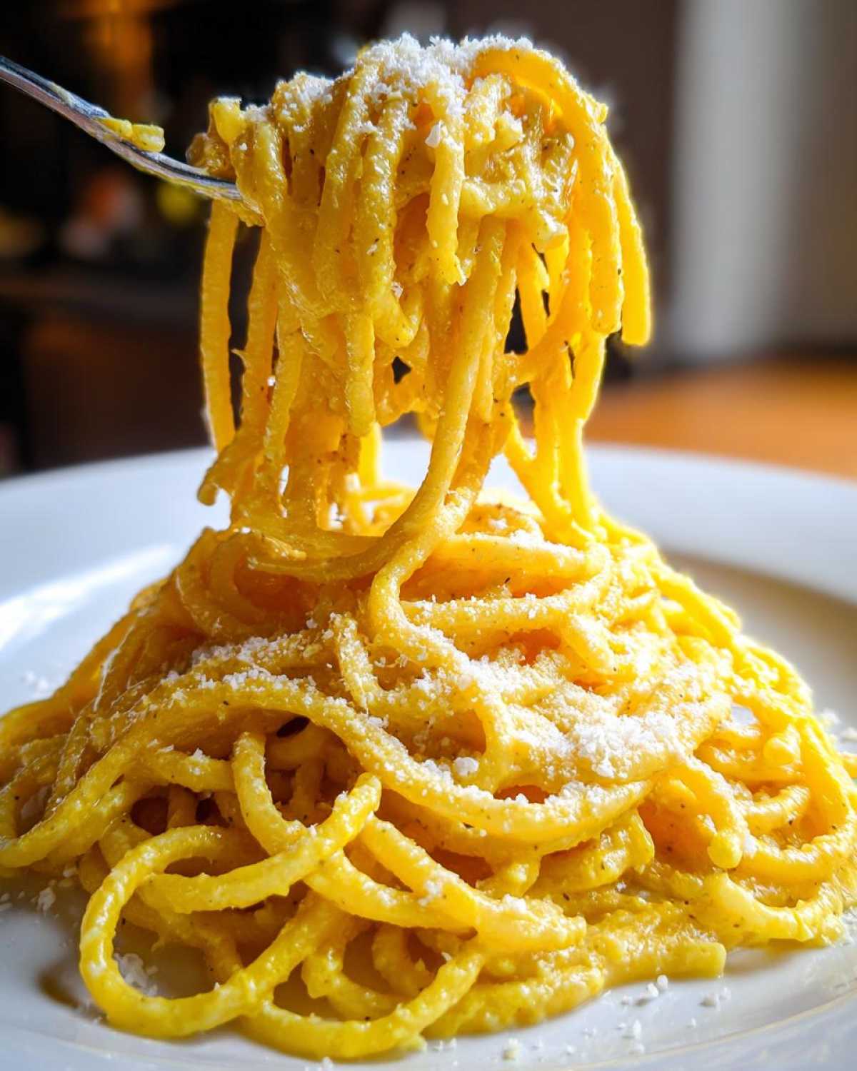 A fork lifts a generous swirl of bright yellow, saucy creamy lemon pasta topped with grated Parmesan cheese.