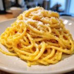 A mound of spaghetti coated in rich, yellow creamy lemon pasta sauce, topped with grated Parmesan cheese.