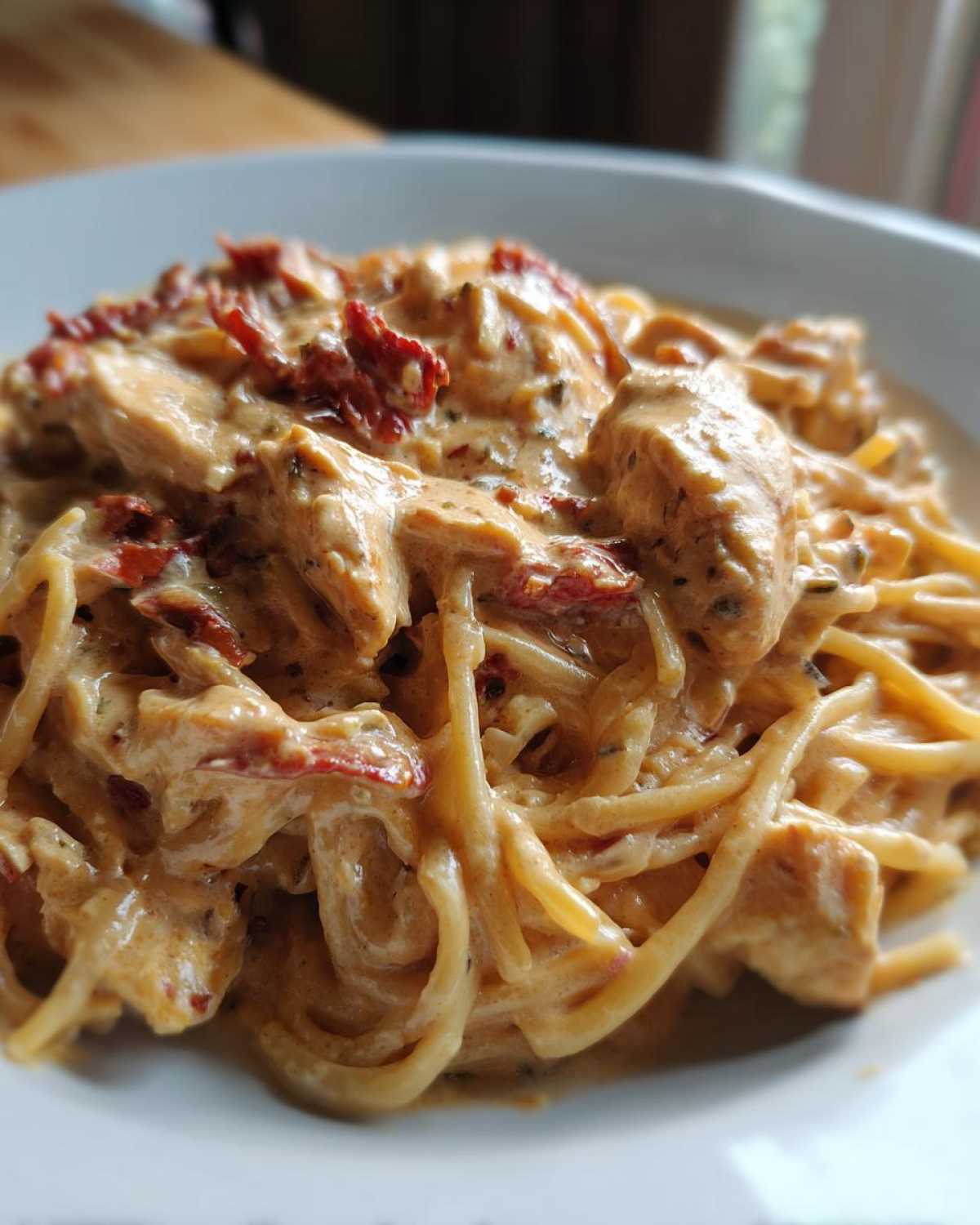 A close-up of creamy marry me chicken pasta featuring chunks of chicken and sun-dried tomatoes coated in a rich sauce.