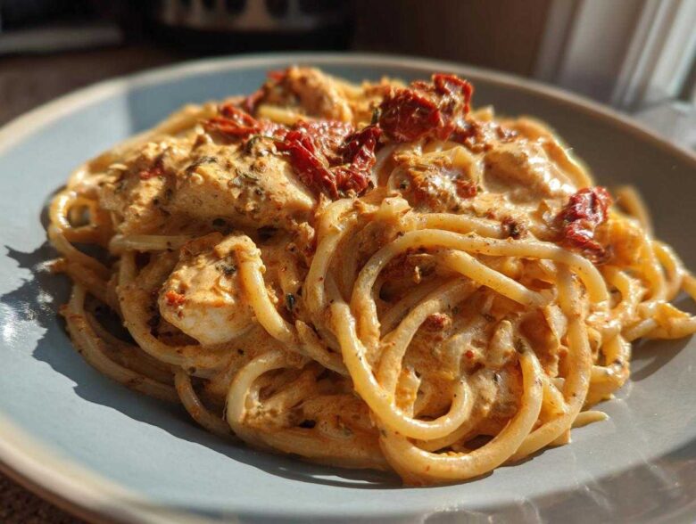 Close-up of creamy marry me chicken pasta topped with sun-dried tomatoes on a light blue plate.