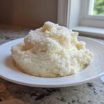 A generous serving of fluffy, creamy mashed potatoes mounded on a white plate.