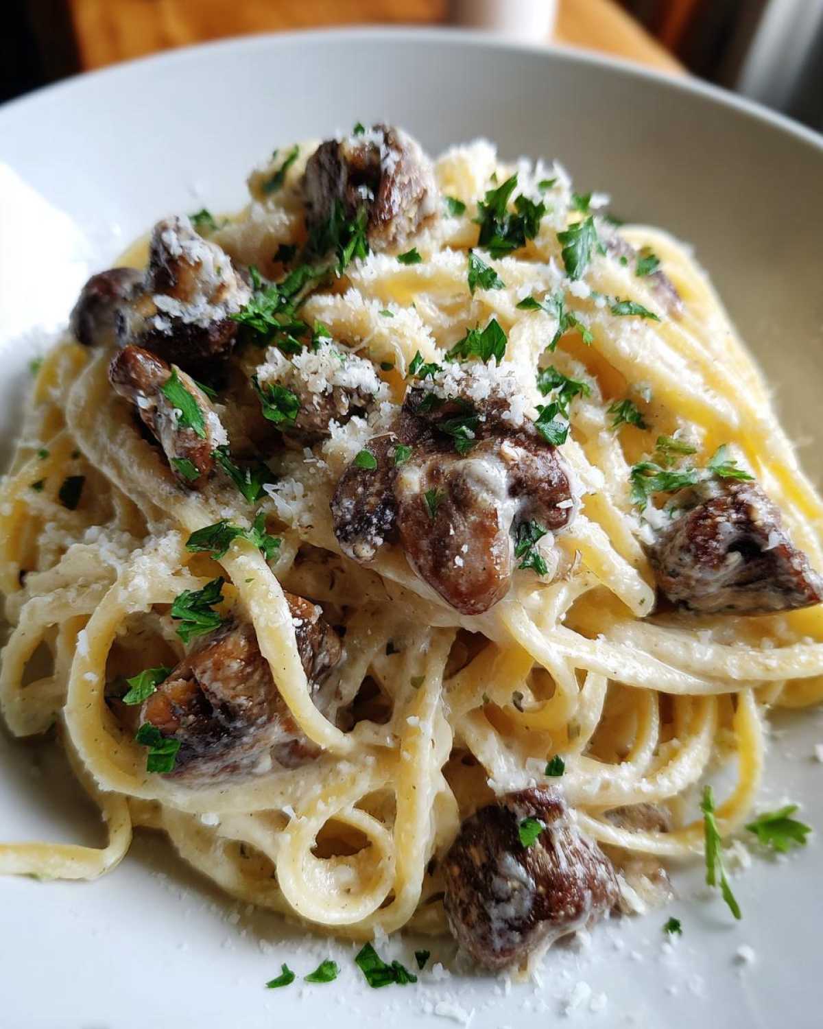 A close-up view of creamy mushroom pasta tossed in a white sauce, topped with sautéed mushrooms, grated cheese, and fresh parsley.