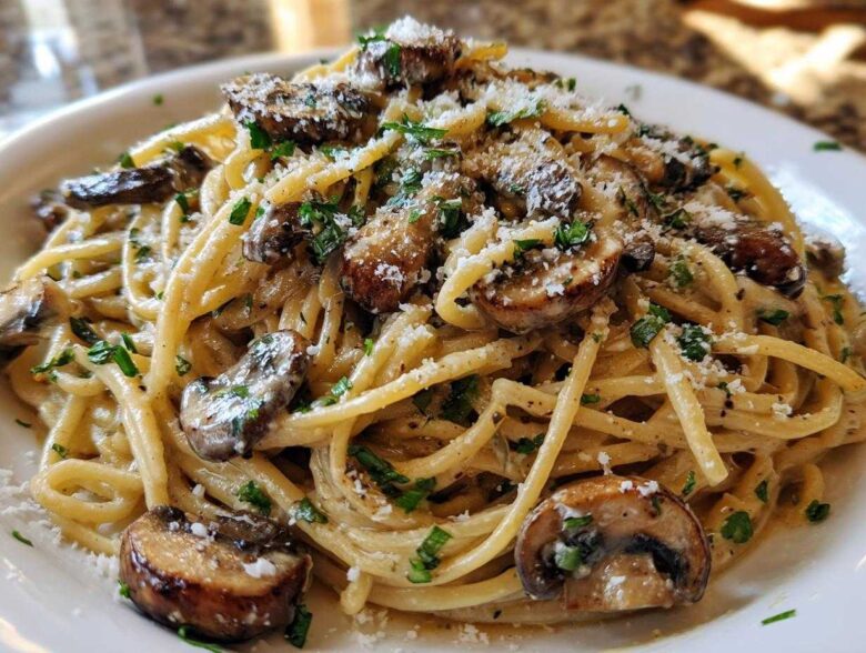 A close-up shot of creamy mushroom pasta tossed in a white sauce, topped with sautéed mushrooms, fresh parsley, and grated Parmesan cheese.