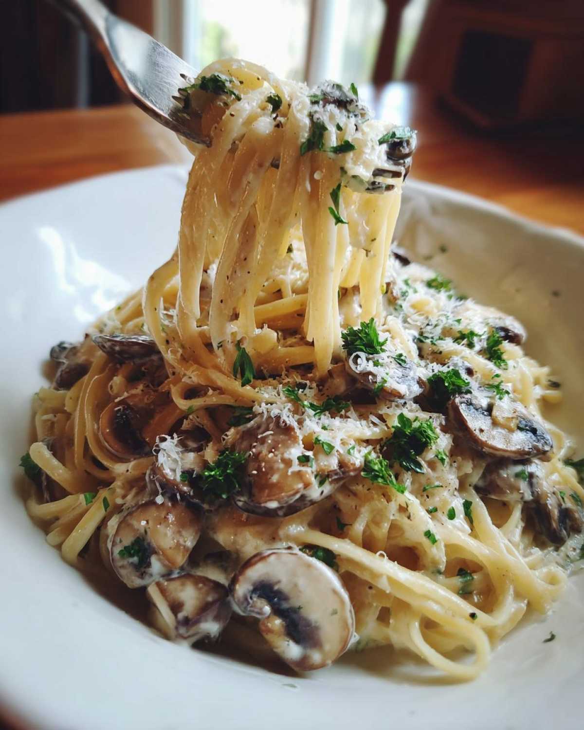 A fork lifts creamy mushroom pasta coated in sauce, garnished with fresh parsley and Parmesan cheese.