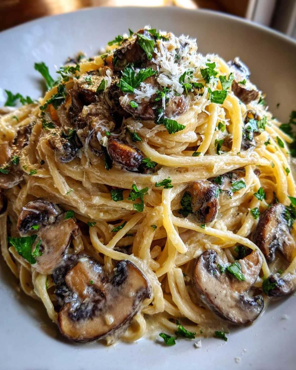 Close-up of creamy mushroom pasta tossed with spaghetti, topped with grated cheese and fresh parsley.