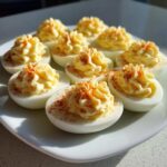 A plate of creamy deviled eggs, piped high with filling and sprinkled with paprika.