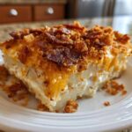 A generous slice of creamy potato casserole topped with melted cheddar cheese and crispy bacon pieces.