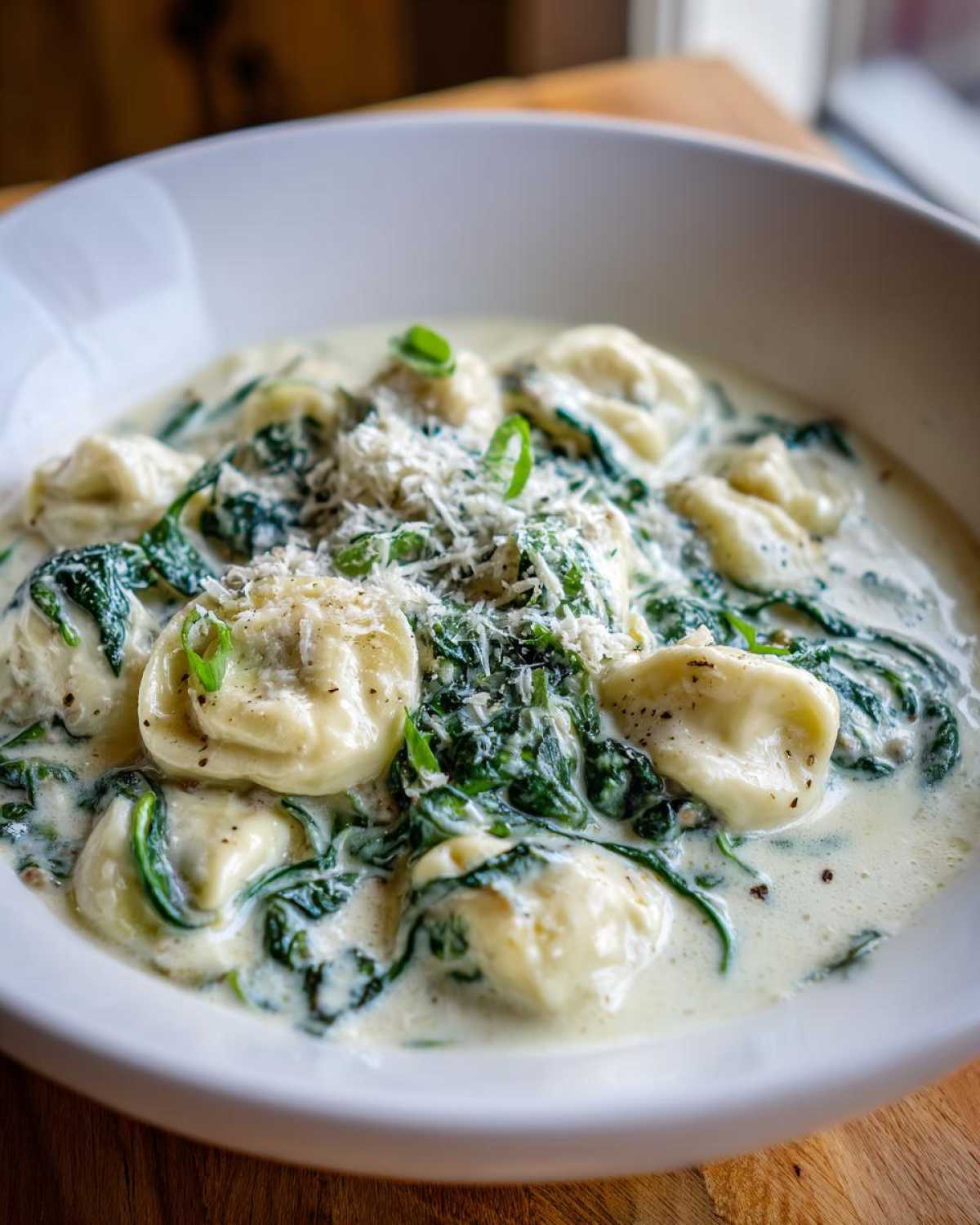 Close-up of creamy tortellini soup with wilted spinach and grated Parmesan cheese topping.