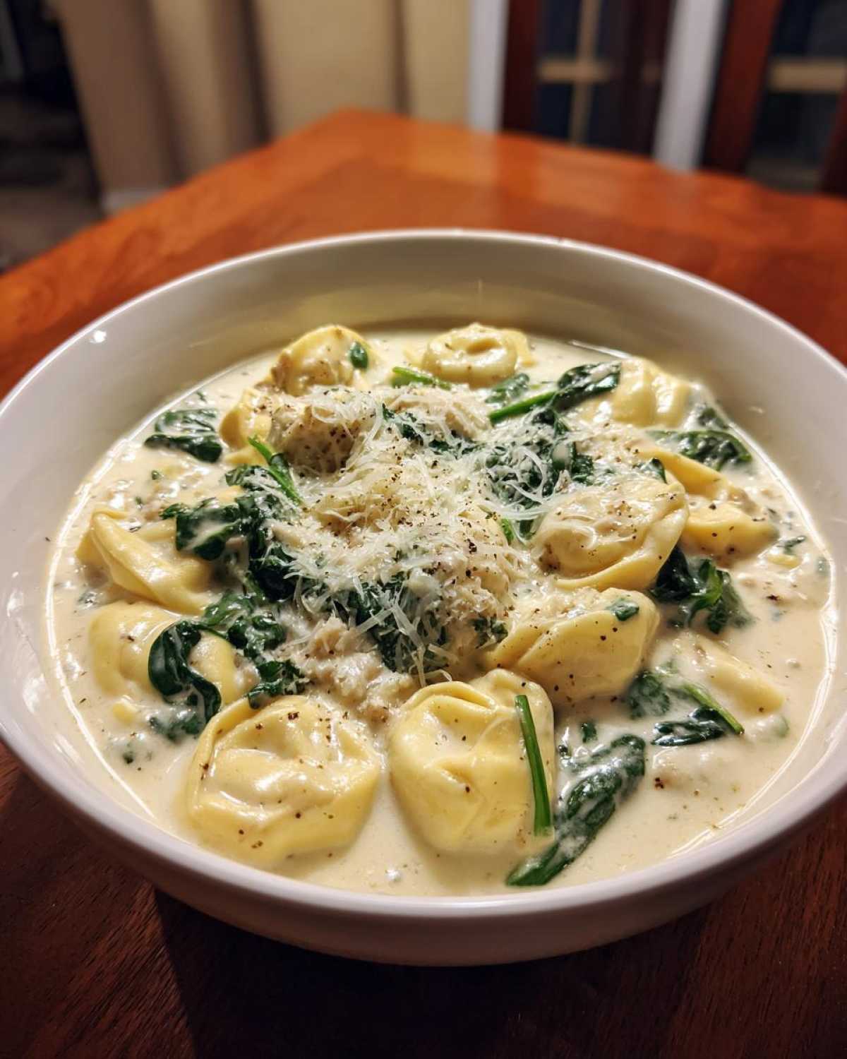 A close-up of a bowl of creamy tortellini soup filled with spinach and topped with grated Parmesan cheese.