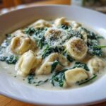 Close-up of a bowl of creamy tortellini soup featuring spinach and topped with grated Parmesan cheese.