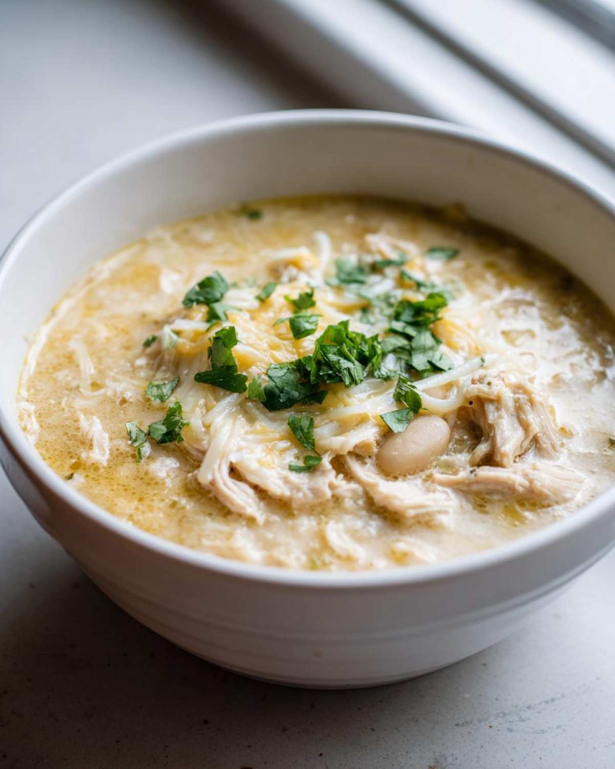 Close-up of a bowl of creamy white chicken chili topped with shredded cheese and fresh cilantro.