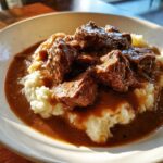 Close-up of tender crockpot beef tips smothered in rich brown gravy served over creamy mashed potatoes.