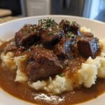 Close-up of tender crockpot beef tips smothered in rich brown gravy served over creamy mashed potatoes.
