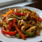 Close-up of seasoned chicken strips mixed with red, green, and yellow peppers and onions for crockpot chicken fajitas.