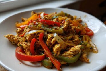 Close-up of seasoned chicken strips mixed with red, green, and yellow peppers and onions for crockpot chicken fajitas.