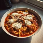 A close-up of a bowl of rich crockpot lasagna soup topped with dollops of ricotta and shredded Parmesan.