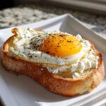 Close-up of delicious egg toast topped with creamy ricotta cheese and cracked pepper.