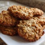A close-up stack of golden brown banana oatmeal cookies piled on a white plate.