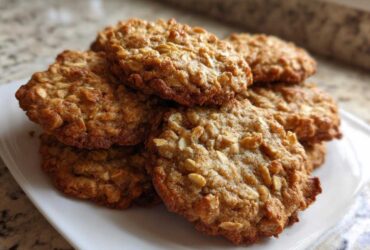 A close-up stack of golden brown banana oatmeal cookies piled on a white plate.