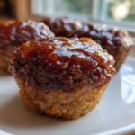 A close-up of a perfectly baked mini meatloaf topped with a shiny, dark orange glaze, resting on a white plate.