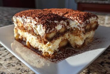 A generous slice of homemade tiramisu recipe, layered with cream and dusted heavily with cocoa powder.