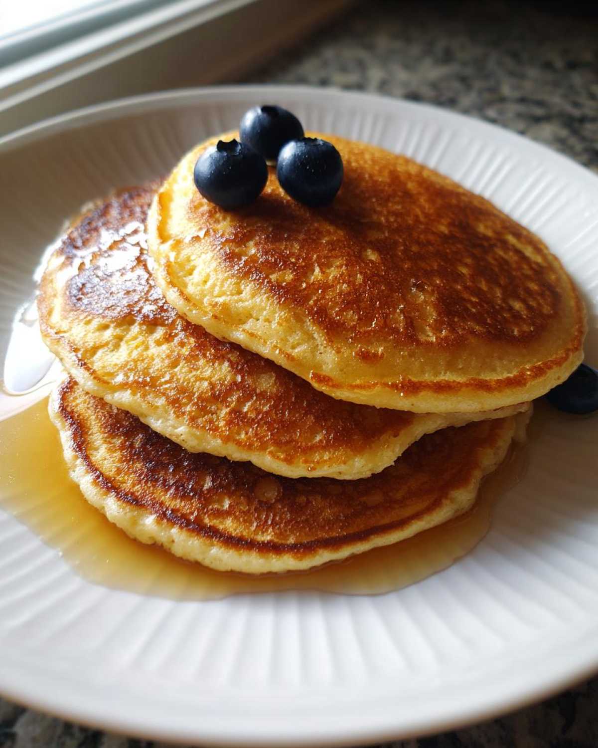 A stack of three fluffy coconut flour pancakes drizzled with syrup and topped with fresh blueberries.