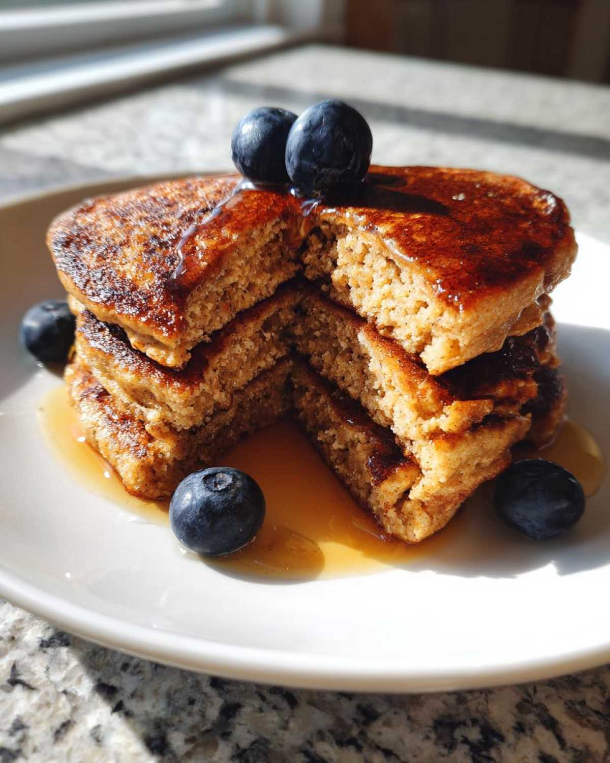 A stack of fluffy coconut flour pancakes cut open, drizzled with syrup and topped with fresh blueberries.