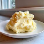 A generous scoop of rich, fluffy creamy mashed potatoes served on a white plate.