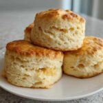 A stack of four tall, fluffy, golden brown scones resting on a white plate.