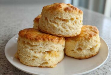 A stack of four tall, fluffy, golden brown scones resting on a white plate.
