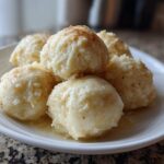A close-up of several fluffy potato dumplings served on a white plate, glistening with melted butter.