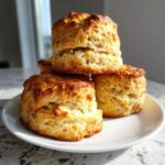 A stack of three perfectly baked, fluffy scones with golden brown tops resting on a white plate.