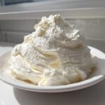 A large mound of fluffy, white vanilla buttercream frosting piled high on a small white plate.