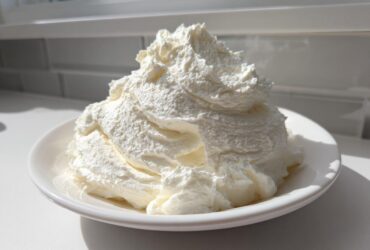 A large mound of fluffy, white vanilla buttercream frosting piled high on a small white plate.