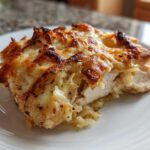 A close-up of a slice of french onion chicken showing tender white meat topped with caramelized onions and bubbly, browned cheese.