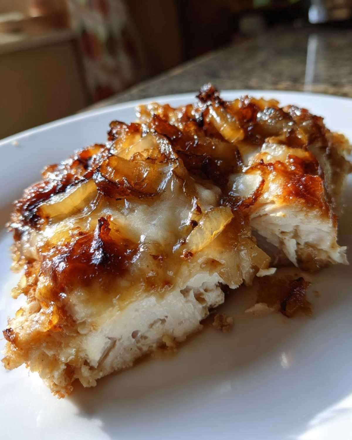 A close-up cross-section of baked french onion chicken topped with caramelized onions and melted cheese.
